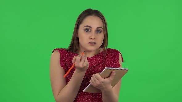 Portrait of Tender Girl in Red Dress Is Angrily Writing with Pencil in Notebook. Green Screen