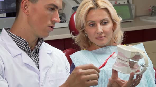 Male Dentist Showing His Patient How To Brush Teeth on a Jaw Mold