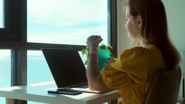 Young Woman Using Laptop Computer at Home and Drinking Clear Fresh Water