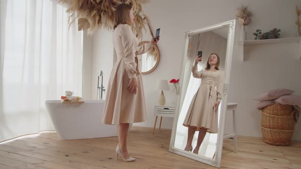 Cheerful Good Looking Woman in New Dress Taking Selfie on Cellphone in Front of Mirror