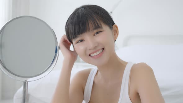 Beautiful face of young asian woman with happy smiling and touch cheek looking mirror.