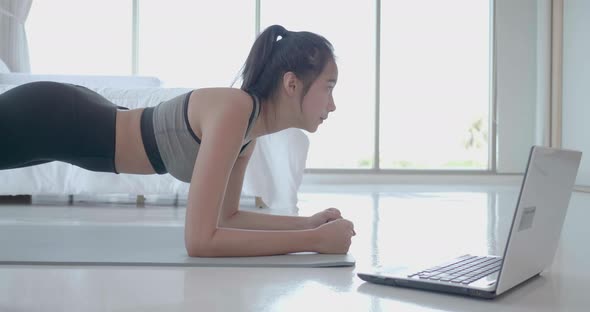 Asian woman exercise workout plank use laptop to watching video digital tutorial at home