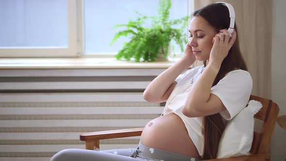 Pregnant Woman Applying Headphones on Belly Sit on Chair Spbd