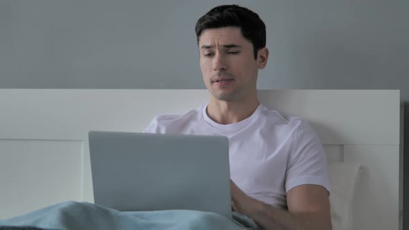 Young Man with Neck Pain Working on Laptop in Bed