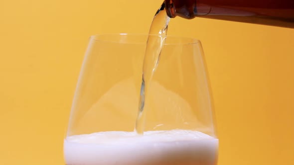 Pouring Beer Into The Glass From Bottle To The Top Close Up View On Yellow Background