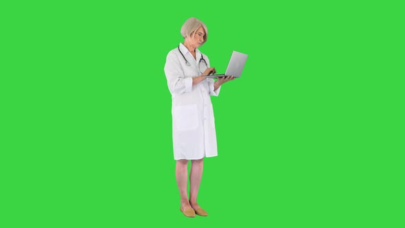 Mature Doctor Woman Standing and Working on a Laptop on a Green Screen Chroma Key