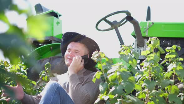 A Young Farmer Communicates on a Smartphone Near His Tractor