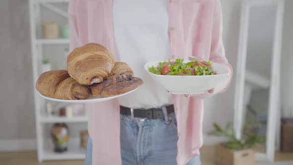 Young Caucasian Woman Holding Plates with Organic Salad and Crusty Croissants