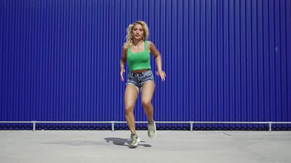 Dancing blond woman in front of blue wall