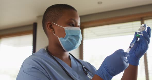 African american female doctor wearing face mask preparing covid vaccine for patient