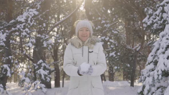 Happy Cute Girl in Winter Clothes Throws Snowball at Camera and Laughs Cheerfully