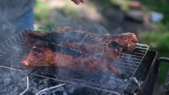 Salting Delicious Beef or Pork Ribs Frying on a Charcoal Grill