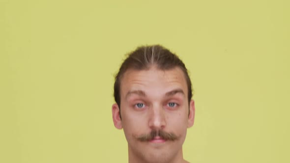 Humorous Appearence of Man with Tied Hair in Front of Camera Over Lemoncoloured Background Closeup