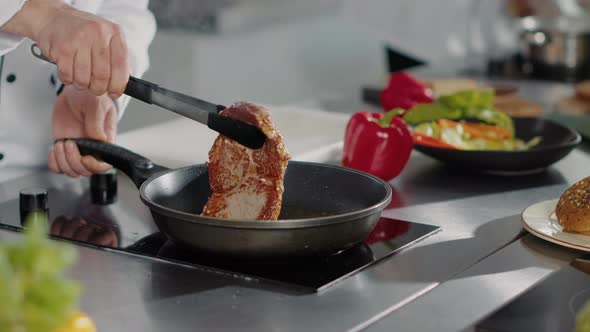 Professional Chef Cooking Pork Steak in Frying Pan on Stove