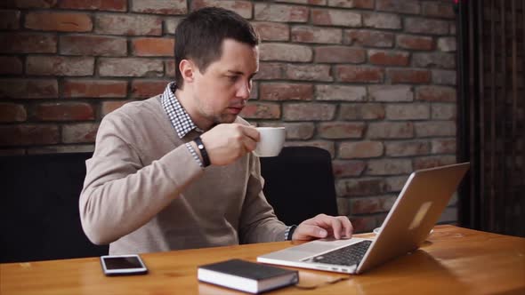 Man Drinking Coffee and Working with Laptop in Cafe