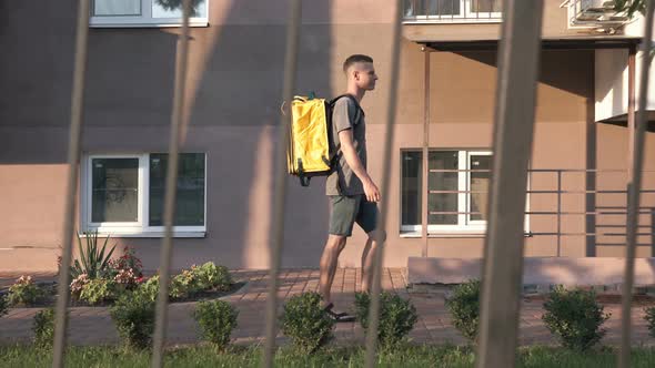 A courier with a yellow backpack delivers an online order. Stay home, self-isolation.