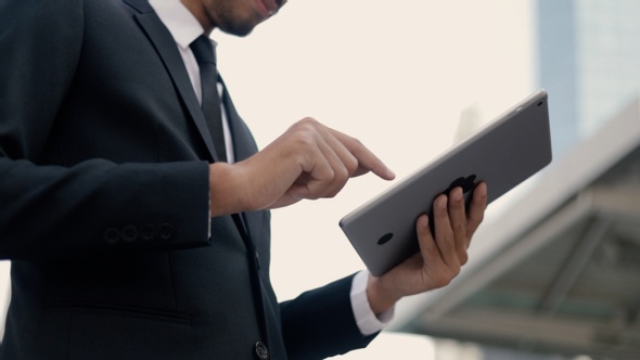 Portrait businessman manager in a black suit using his tablet digital typing message.