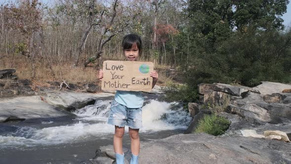 Portrait of cute little girl standing with Love Your Mother Earth poster at a waterfall in the fores