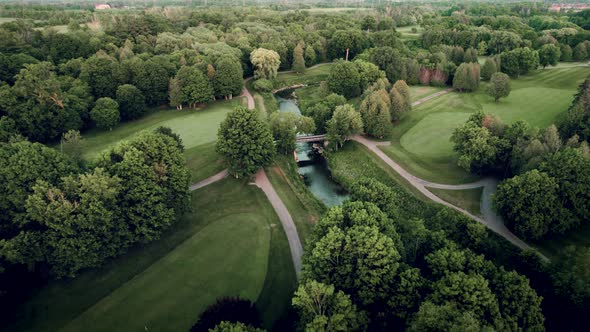 Aerial view of lush scenic golf course with river and bridge drone fly over at sunset in summertime