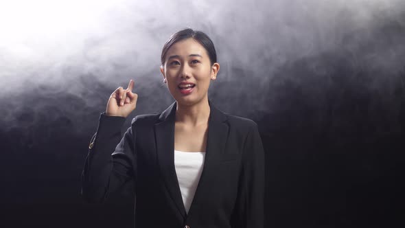 Asian Speaker Woman In Business Suit Showing Index Fingers Up While Speaking On Stage