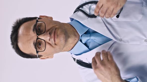 Vertical Shot Handsome Male Doctor in Medical Coat Puts on Stethoscope and Smiles
