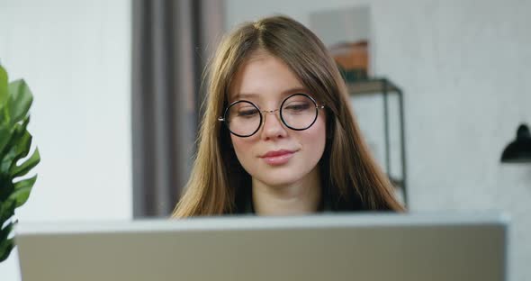Young Female Worker in Eyeglasses Working on Laptop at Home at Daytime
