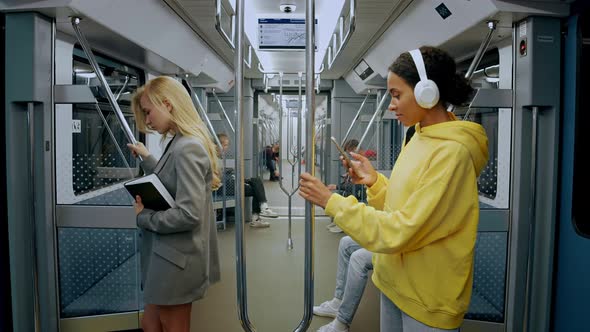 Young Girls Standing in Metro Train One Wearing Headphones and Looking in Phone