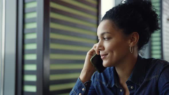 Young African American Woman Talking on Phone Sitting at the Tables in the Cafe of the Mall