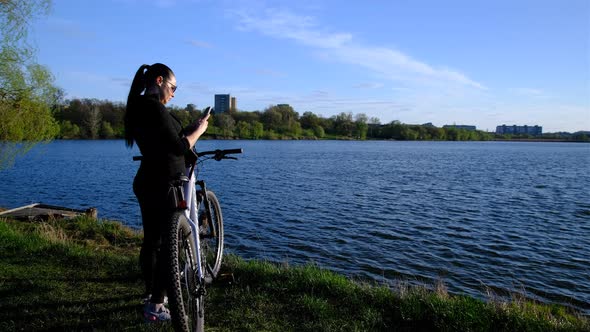 a woman with bicycle walking to lake, river in sunset time.