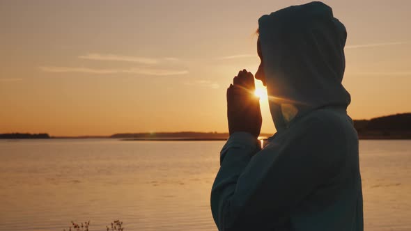 Silhouette of a Woman Praying at Sunset By the Lake