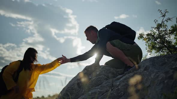 A Man Helps a Woman Climb a Rock in the Mountains