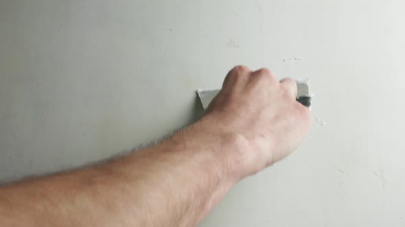 Hand with a spatula smooths out the unevenness of the concrete wall.