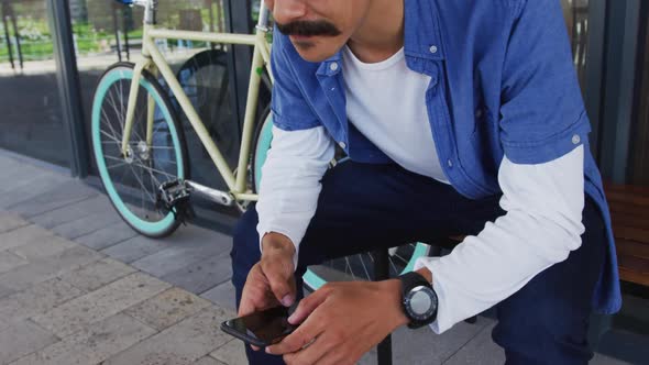 Mixed race man with moustache sitting in street using smartphone