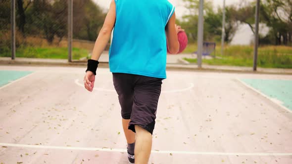 Back View of Young Man Playing Basketball He is Jumping Up and Throwing a Ball to the Basket