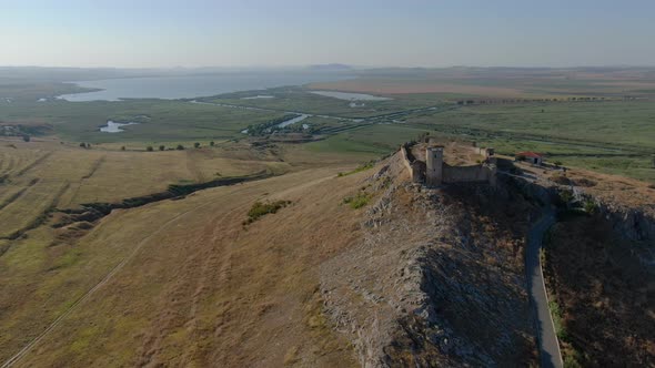 Drone tracking shot with front side of Enisala, medieval fortress on top of a hill surrounded by lak