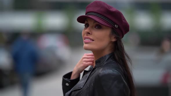 Portrait of a Brunette with Long Hair in a Black Leather Jacket and a Burgundy Cap Against the