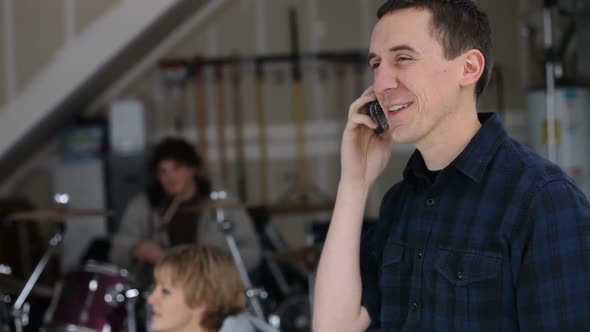 Young man in garage with band talking on cell phone