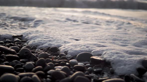 Close up beach waves and foam bubbling through pebbles and rocks slowmo