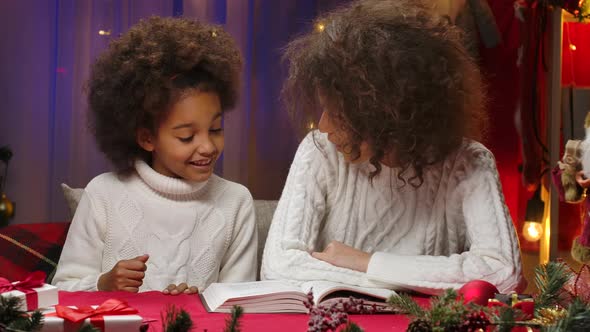 African American Mom and Little Daughter in White Sweaters Read a Book and Cuddle Happily