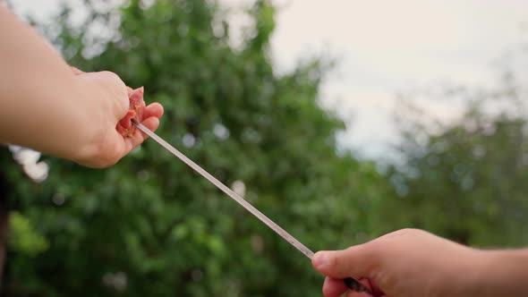 Male chef putting pieces meat on skewer closeup outdoors. Man's hands string raw beef