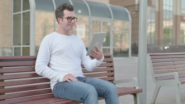 Online Video Chat on Tablet By Young Man Sitting Outdoor on Bench