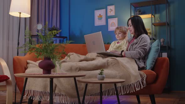 Mother and Small Child Daughter Kid Study at Laptop Watching Funny Movies Relaxing Lying on Sofa