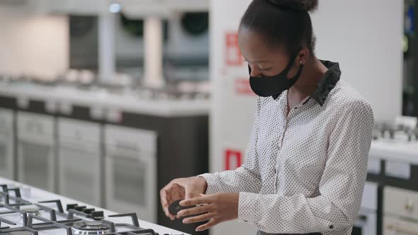 Young Black Woman with Face Mask is Choosing Gas Stove in Home Appliance Stores in Mall Shopping