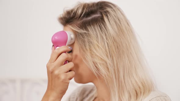 Blond Caucasian Woman Cleaning Her Face with an Electric Brush Closeup Isolated