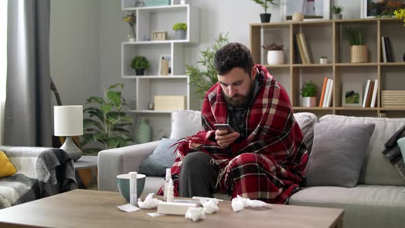 Ill Man Uses a Smartphone at Home on the Sofa