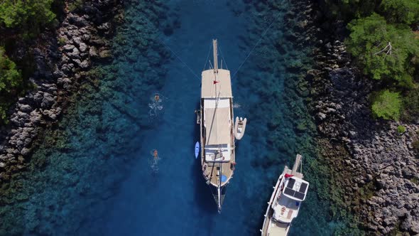 Large Boat is Moored in the Sea Strait with Reef Bottom and Tourists Swim Near It Filmed From Above