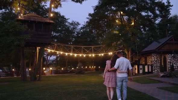 Back Frame with Two Young Romantics Walking Embracing. Happy Couple Walking on an Illuminated Park