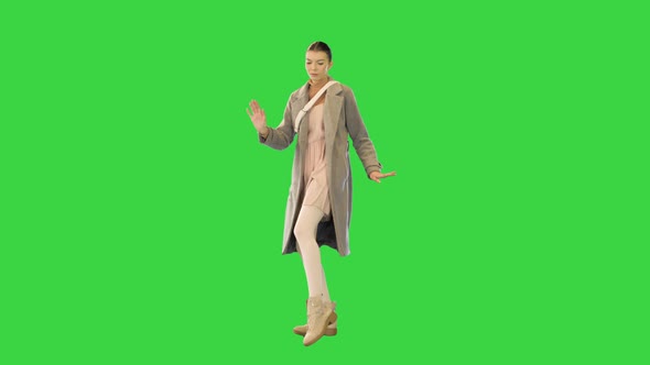 Young Woman in Grey Coat Stands Dancing on a Green Screen Chroma Key