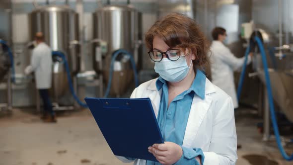 Scientist in Mask and Coat with Clipboard Working at Craft Brewery or Beer Plant