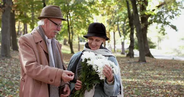 Happy Retired Couple Having Fun Talk She Sniffing a Bouquet of Flowers in Park